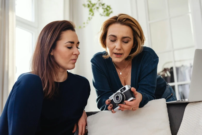 two women look at a camera together, while using the phone