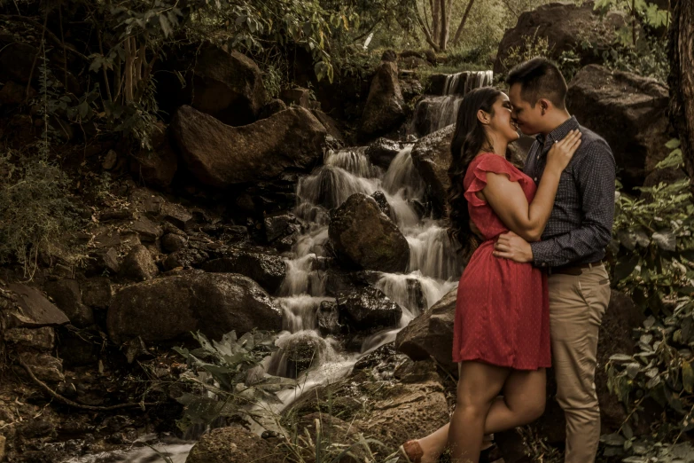 two people are kissing next to a waterfall