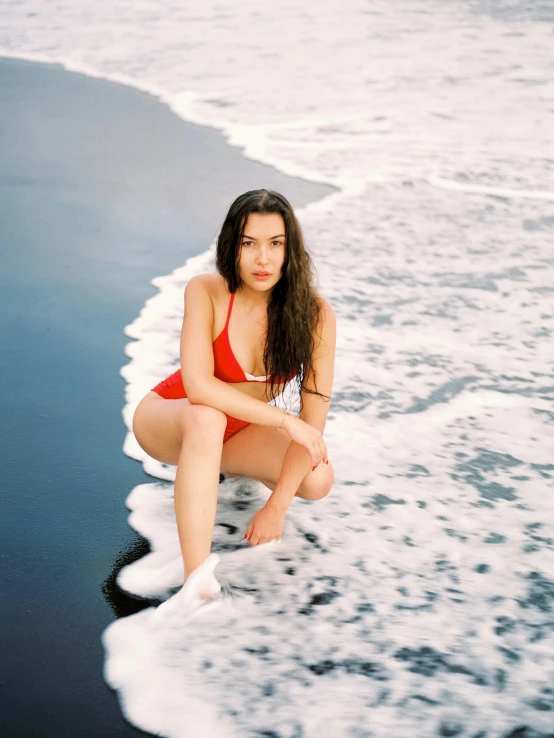 a young woman in a red swimsuit crouches down while sitting on the beach