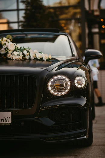 the front end of a black bentley with flowers on it