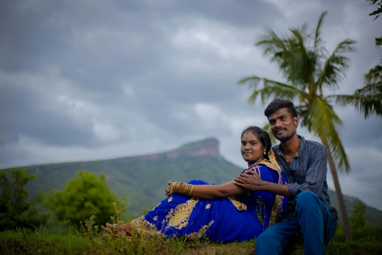 a couple sit on a field near some mountains