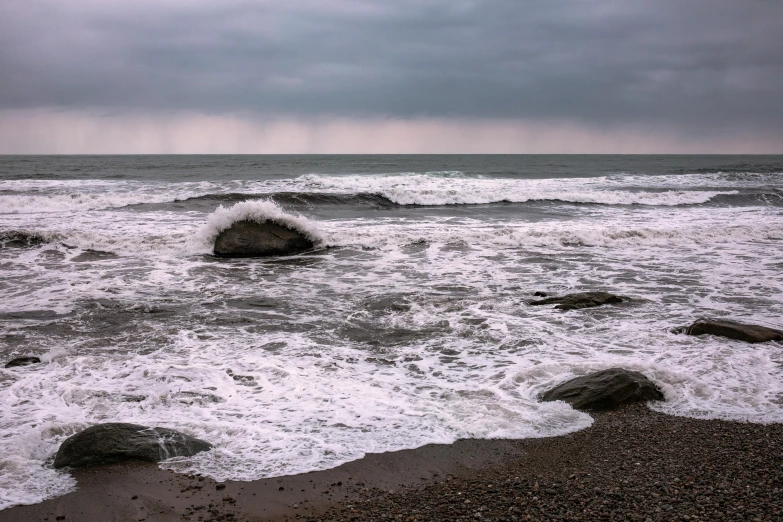 a lone surfer sits atop the rocks of a surfboard as it breaks out into the ocean