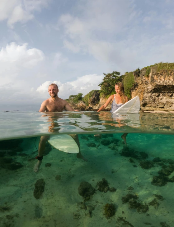 a young man and woman paddling surfboards in shallow water