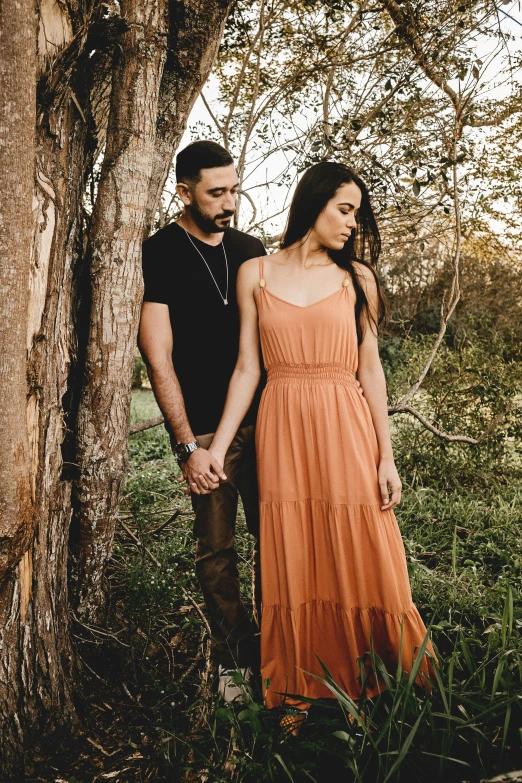 an adult man and woman are holding hands while leaning against a tree