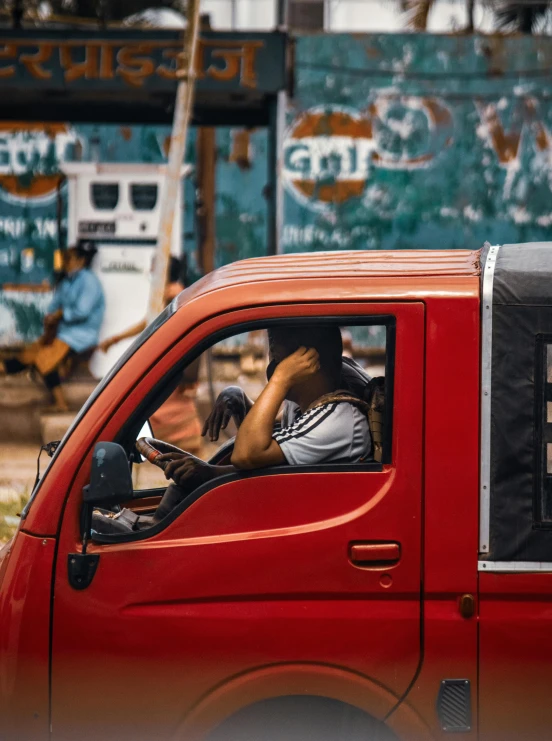 the man sits in the cab of his red truck