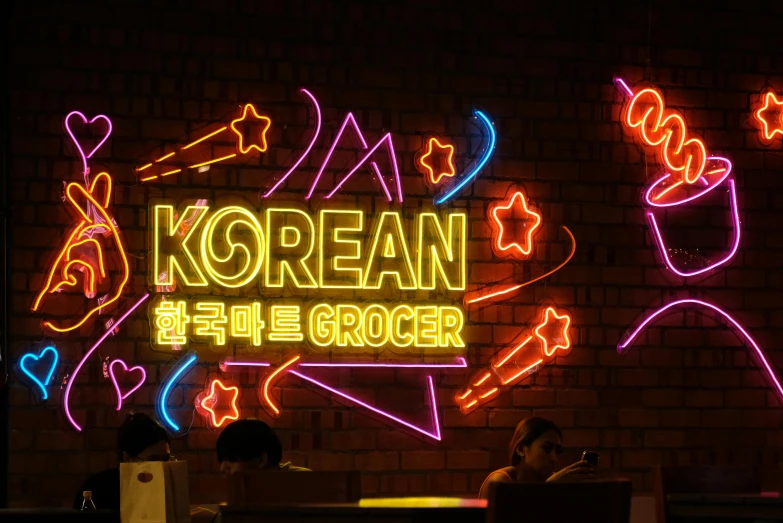 a neon korean food store sign in front of a brick wall