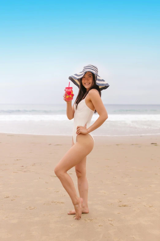 girl in white at beach with hat holding a drink