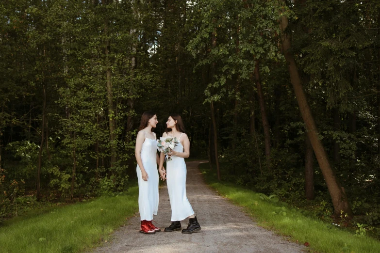a pair of women are dressed in white as they stand on a road