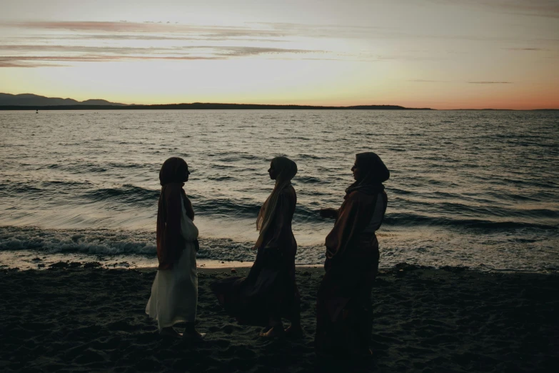 four people on the beach are standing next to the water