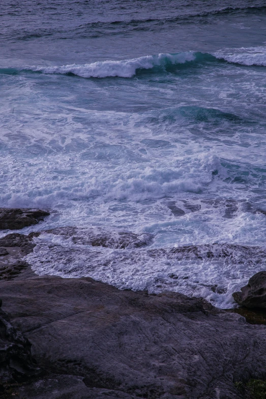 the person is sitting on the rocks looking out to sea