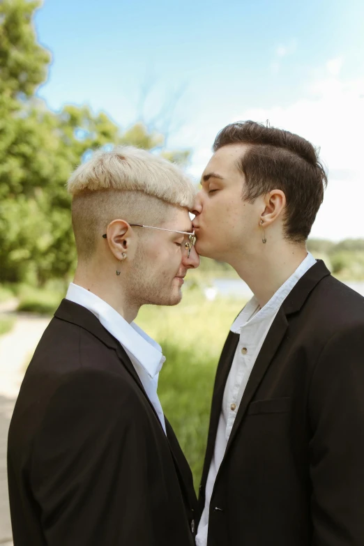 two males kissing each other in front of some trees