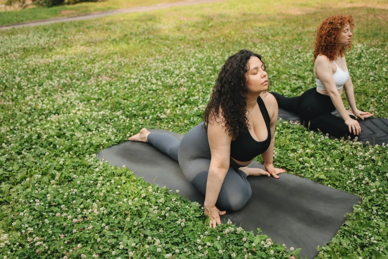 two women are sitting on mats doing yoga outdoors