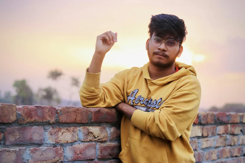 an indian man with his arm crossed leaning against a brick wall