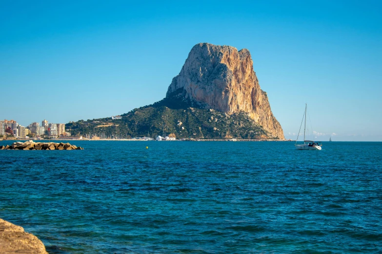 a sail boat floating on the water next to a hill