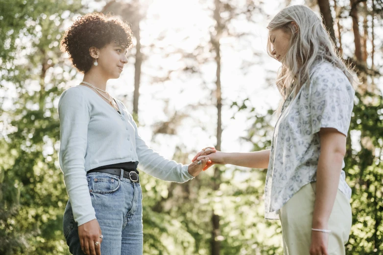 two women looking at each other with woods in the background