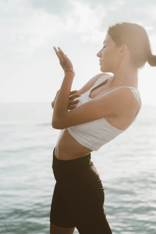 woman looking back with arms stretched, standing at ocean