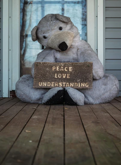 a white teddy bear holding a sign that says peace love rare starting