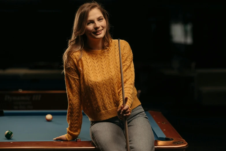 a woman sitting on a pool table in front of a pool cue