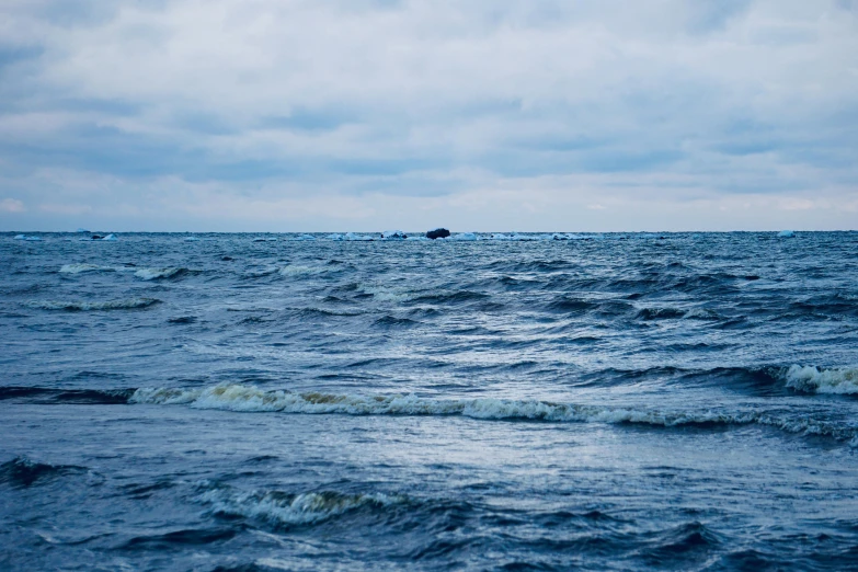 small boat in large choppy ocean under cloudy sky