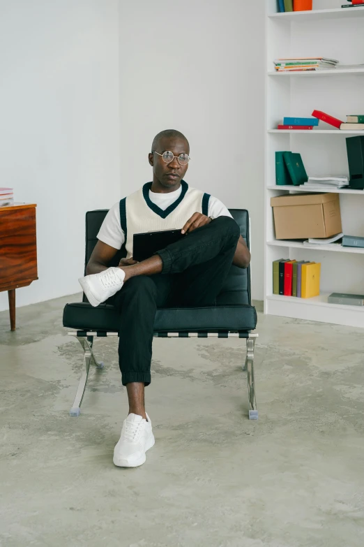 a young man sits in a chair with his feet crossed