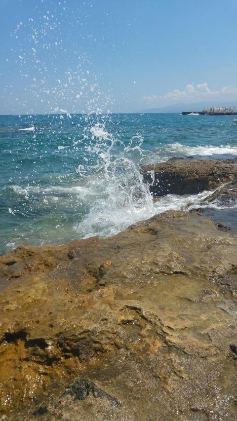 an ocean splash near rocks on a sunny day