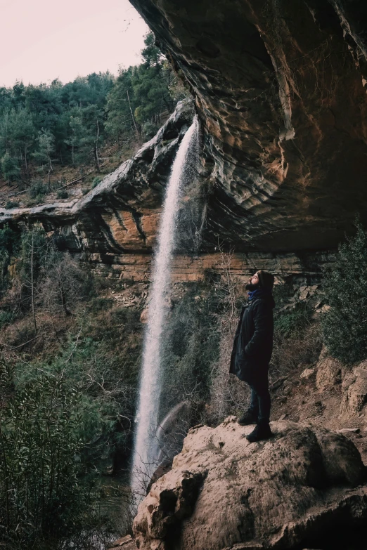 the young man is standing near the water that's flowing down the cliff