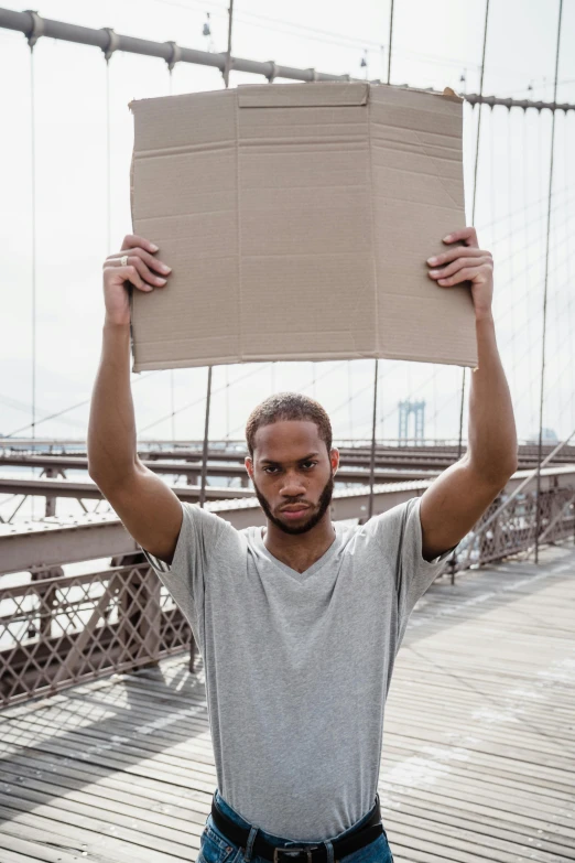 a man holds up a cardboard board on a bridge