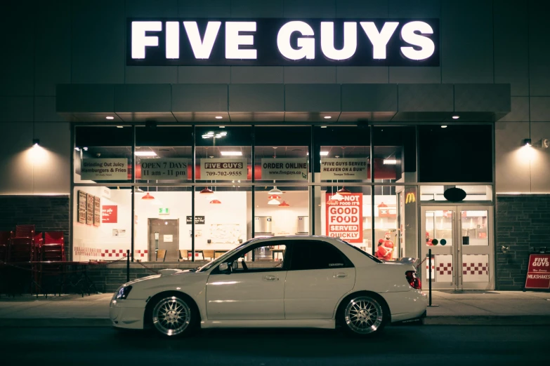 a small car parked outside of a five guys store
