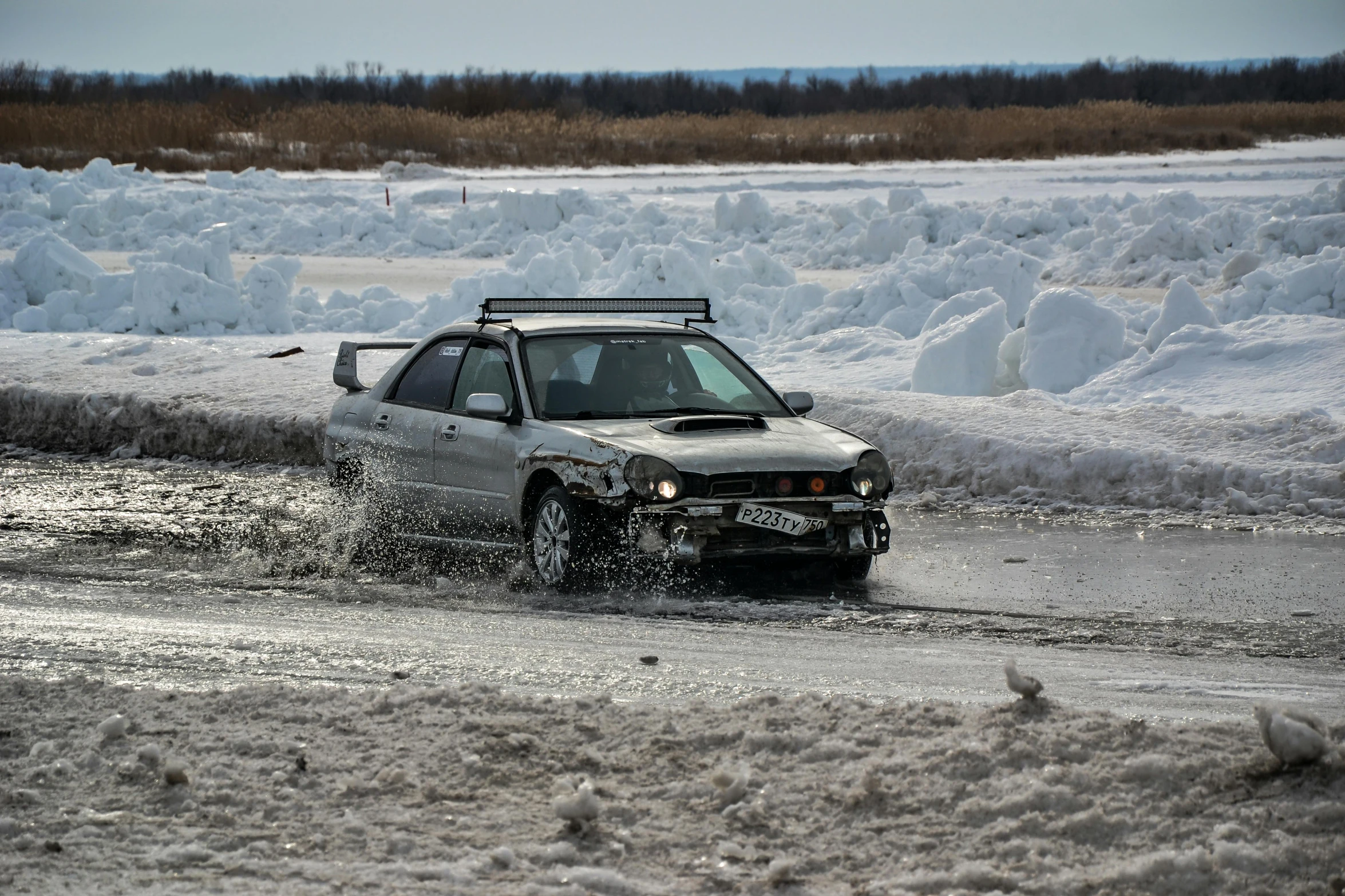 a white suv driving down a wet road near snow