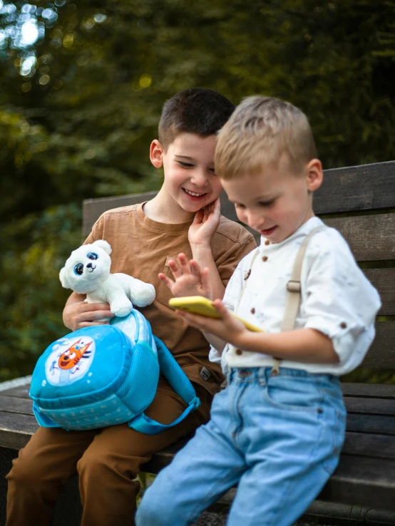 two little boys sitting on a park bench playing with a stuffed animal