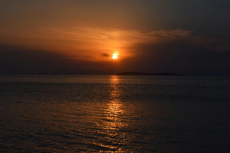 a sunset view of the sun behind a boat sailing in the ocean