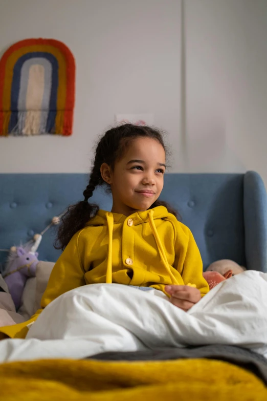 a  sitting on top of a bed in a yellow hoodie