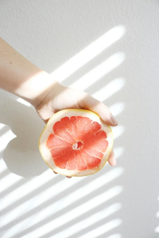 someone holding a gfruit half in front of a white wall