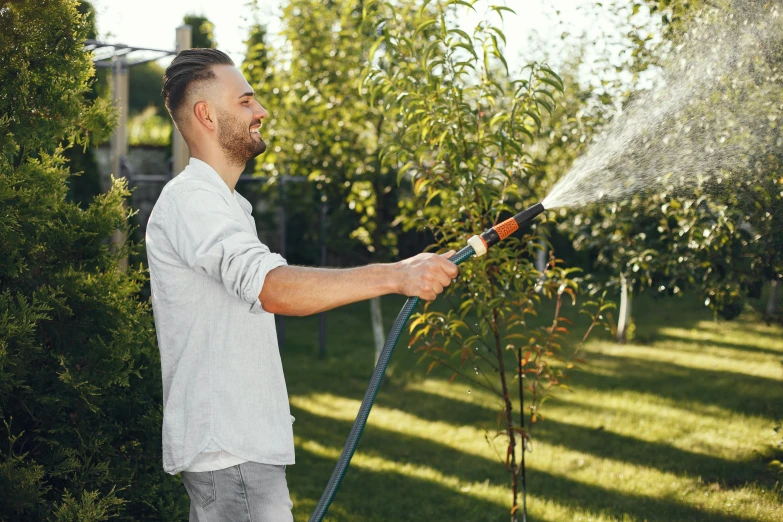 a man in a white shirt uses a pressure gun to spray water from a tree