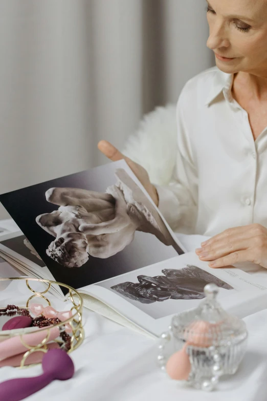 a woman holds an open book and examines the pages with some beaded accessories