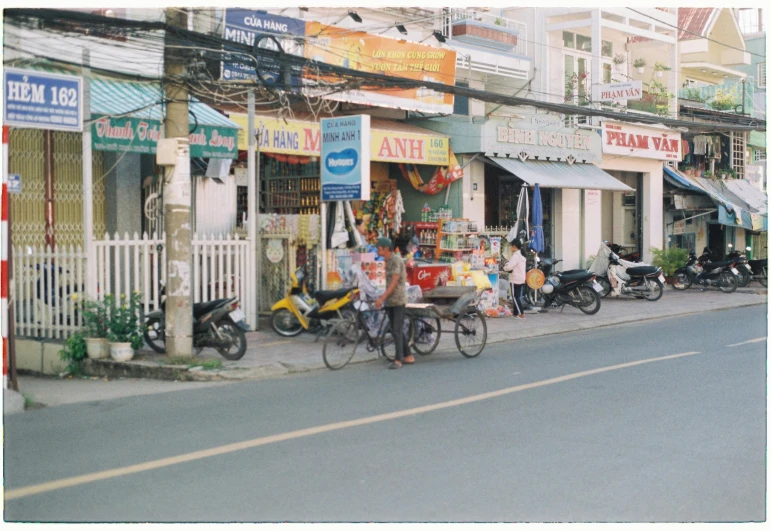 a woman is walking her bike by some shops