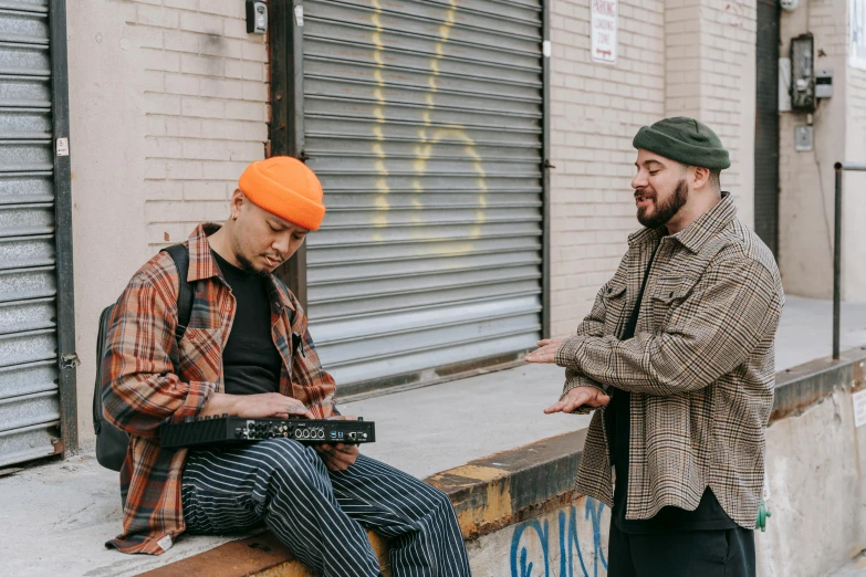 two young men standing next to a brick wall, one wearing an orange cap