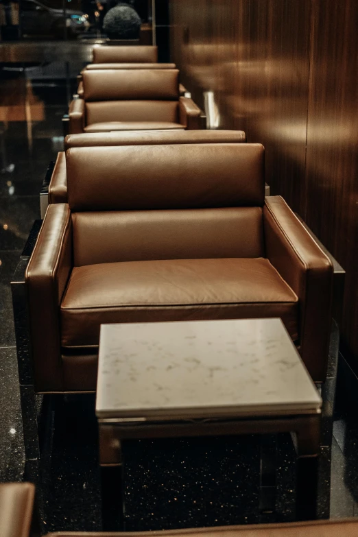 three brown chairs and a side table are lined up against the wall