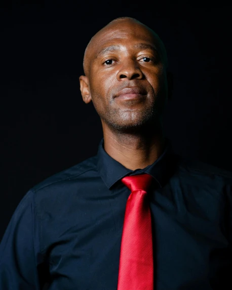 man wearing a dark blue shirt and red tie with a black background