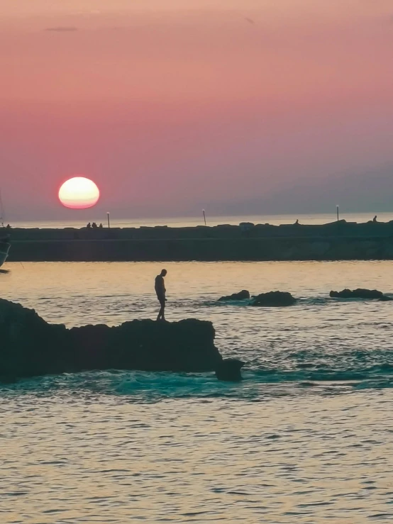 a person standing on the rocks near the ocean with a boat