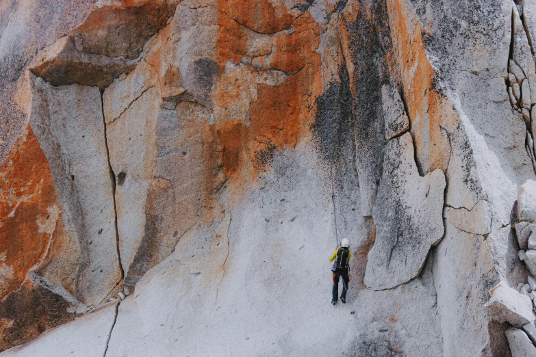 an aerial s of a person climbing up an orange and gray cliff