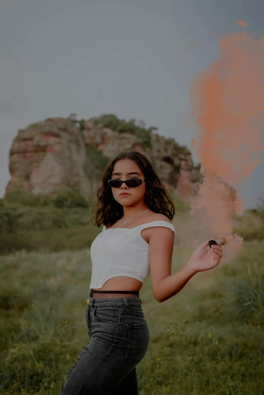 a woman in high - rise jeans, black eyeliners and shades is holding a cigarette