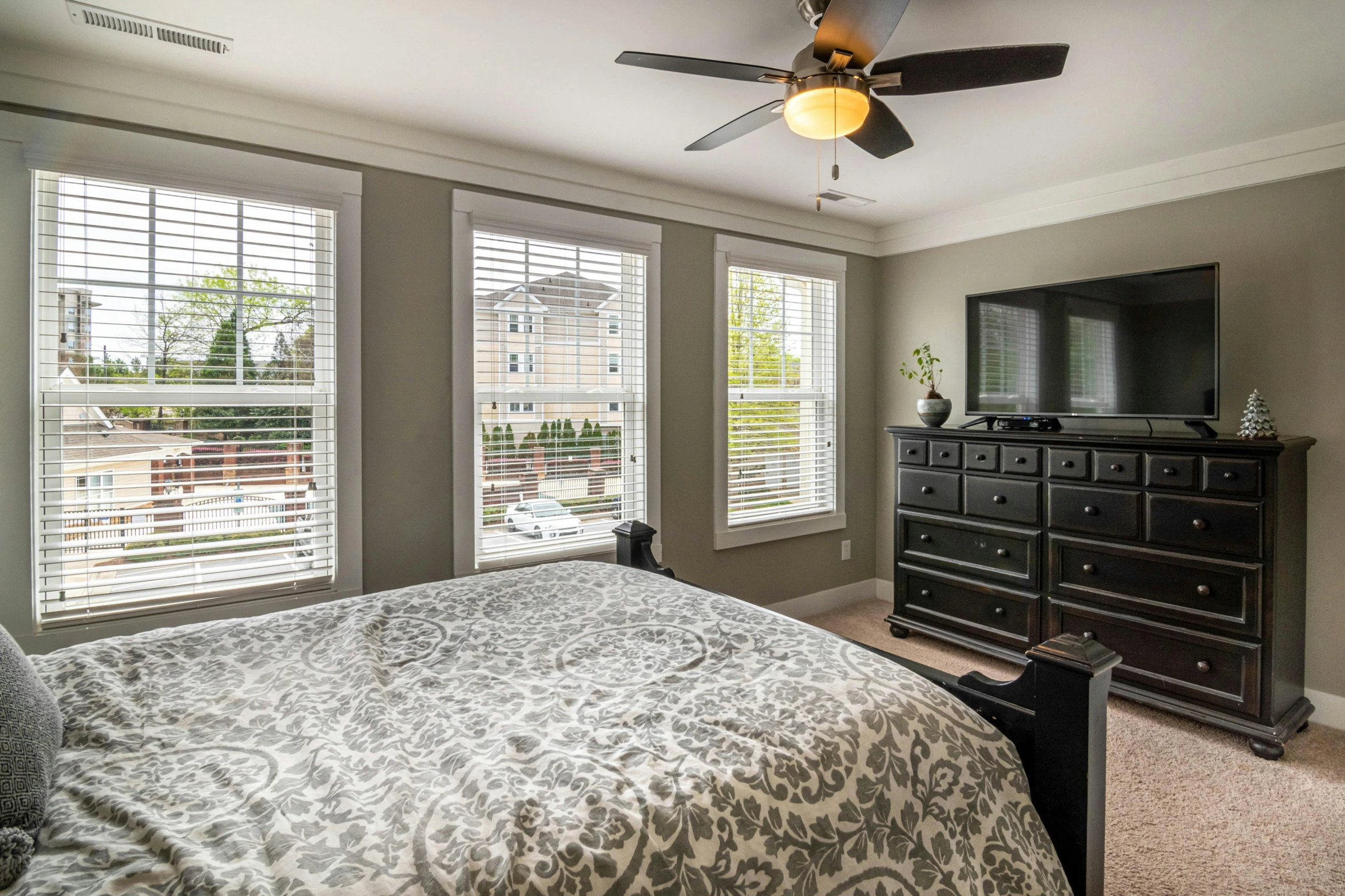 a master bedroom with large windows has grey bedding