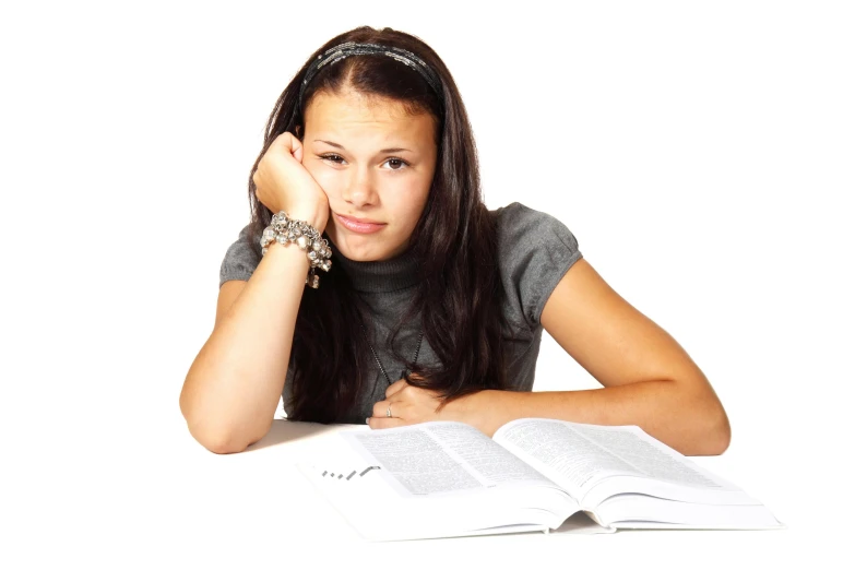 a girl sitting at a table with a book and pen