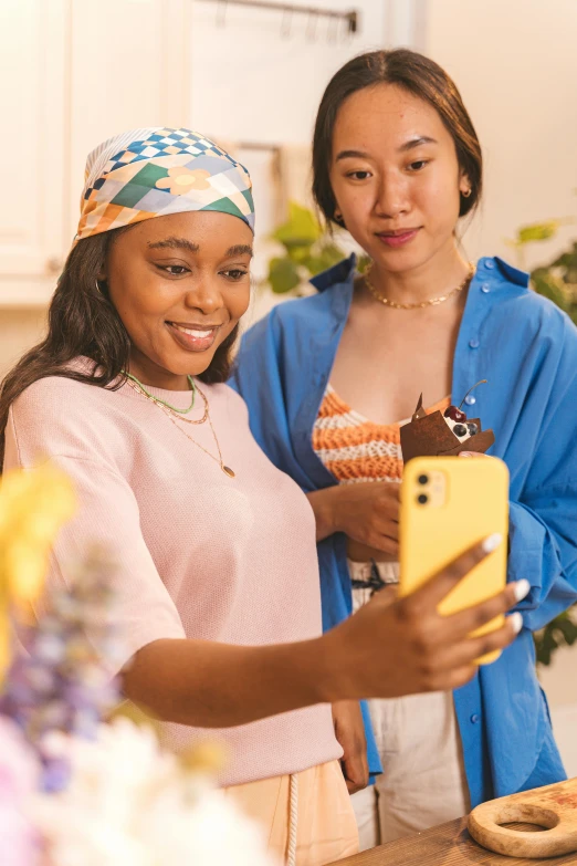 two women in a kitchen with one holding up a cake and the other holding her phone