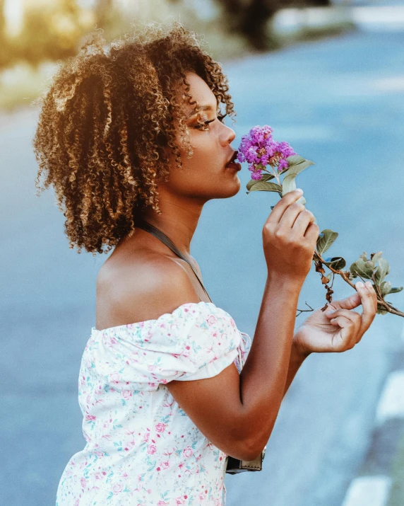 a woman smelling some purple flowers outside in the sun