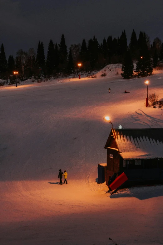 two people on the snow by a ski lodge at night