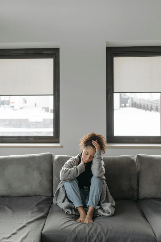 a woman sitting on a grey couch in front of windows