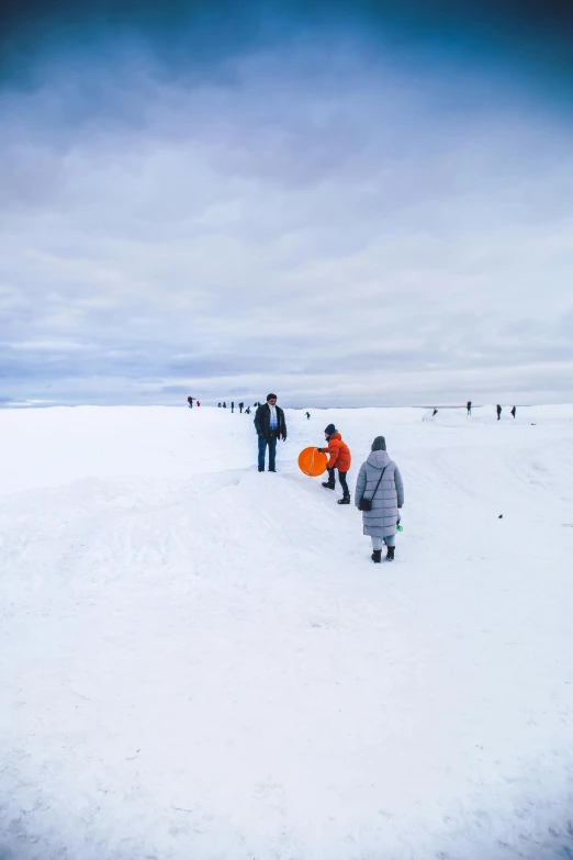 several people are out in the snow carrying an orange surfboard