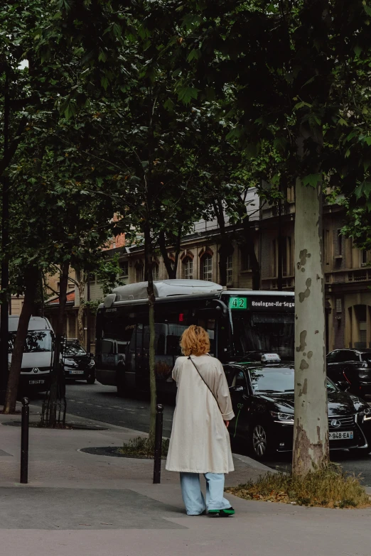 a woman is standing next to a tree waiting on a bus